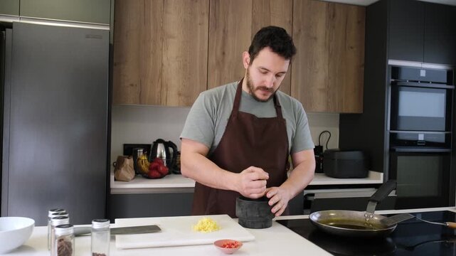 Male cook in an apron using a mortar and pestle to crush spices in a modern kitchen