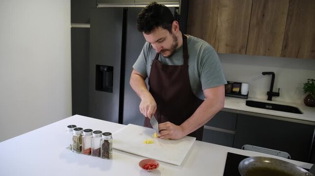 Man wearing an apron carefully mincing fresh ginger on a white cutting board