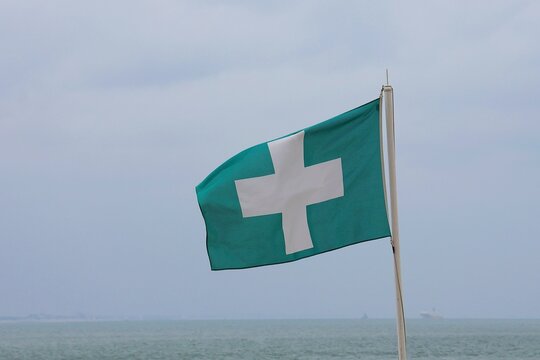 Close-up of a waving green flag with a white cross. First aid station on the beach.