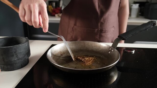 Male cook stirring and roasting a mix of fragrant spices in a hot pan on an induction stove