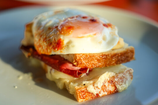 Close‑up of a Croque Madame sandwich with melted cheese, cured ham, and a fried egg on toasted bread, capturing rich textures and warm golden tones in natural light.