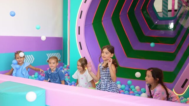 Group of excited girls joyfully playing together and throwing balls in a large ball pit