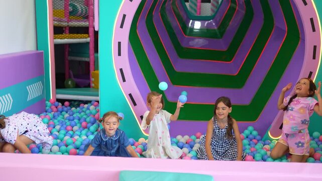 Slow motion footage of happy girls throwing colorful balls in a playground ball pit