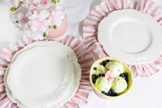 A serving of pistachio-mint ice cream with blueberries on a white plate with floral decorations in pink pastel colors