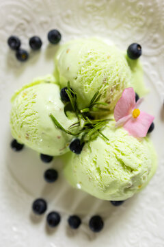 A serving of pistachio-mint ice cream with blueberries on a white plate with floral decorations in pink pastel colors