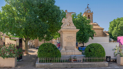 Obraz premium Puimoisson, France - 07 05 2026: Panoramic view of the main square with war memorial, Saint-Michel Church and the fairground all around of the hilltop village under a blue sunny sky