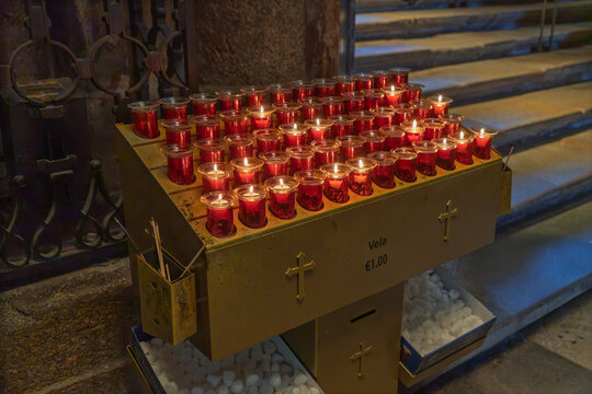 Rows of burning votive candles illuminating a metal stand in a religious setting, symbolizing prayer and devotion