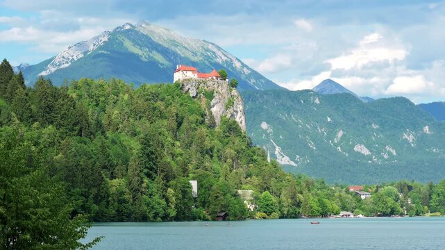 Scenic view of Bled Castle perched on a towering cliff above Lake Bled, Slovenia, with boats on the lake and the majestic Julian Alps rising in the background.