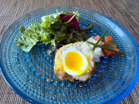 Half boiled cooked egg on fresh bread and salad with vegetables for a health diet breakfast on blue plate