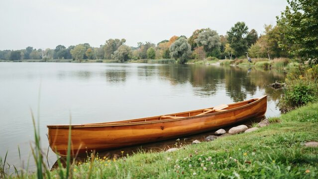 Wooden canoe resting on grassy shore of calm lake surrounded by autumn trees
