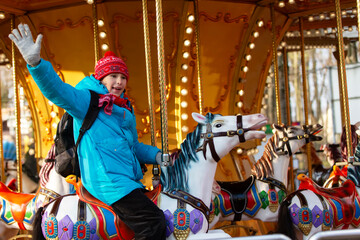 A schoolboy boy with a backpack waves his hand on a carousel in a brightly lit amusement park © Светлана Лазаренко