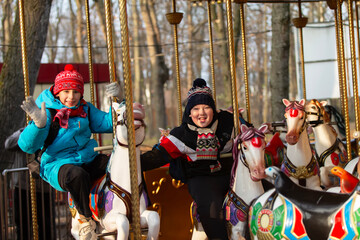 Two school-age children in winter clothes ride on a carousel in the park in autumn © Светлана Лазаренко
