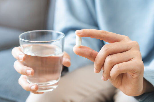 Sick, asian young woman, girl hand holding pill, painkiller medicine from stomach pain, headache, pain for treatment, take drug or vitamin and glass of water at home, pharmacy and health care concept.