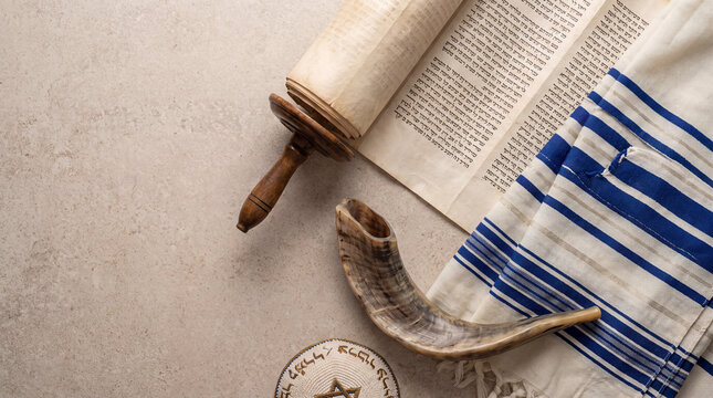 A high-angle view featuring a Torah scroll, a shofar, a tallit prayer shawl, and a kippah on a stone background, representing Jewish religious traditions.
