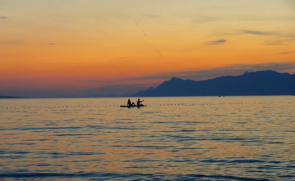 Silhouettes of a young couple in love on a surfboard in romantic sunset on the sea, water activities background