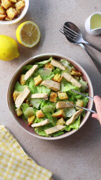 Overhead video of a hand pouring creamy Caesar dressing over a homemade Caesar salad with grilled chicken, Parmesan cheese and croutons. Flat lay cooking scene. Vertical video.