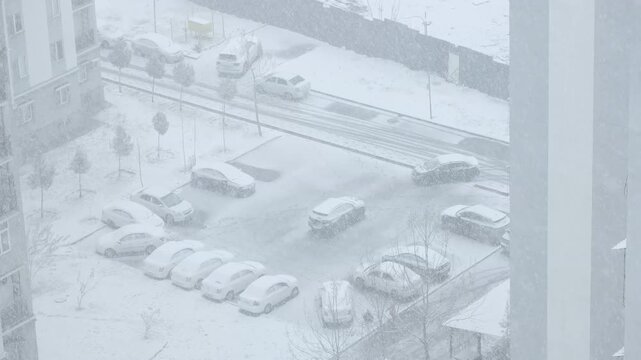 High angle aerial view of a car pulling into a snow-covered residential parking lot during a heavy winter blizzard, real-time 60fps.