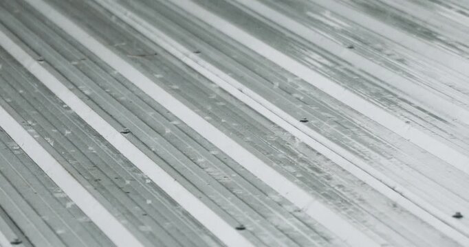 Rain falling on a metal roof with water flowing across the surface, illustrating wet weather, rainy season, construction materials, moisture, and outdoor environmental conditions