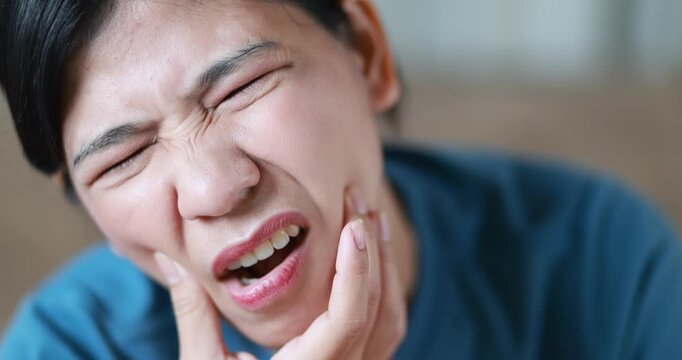 Woman suffering from toothache, holding her cheek in pain, tooth pain, dental problems, oral health, tooth sensitivity, cavity, dental treatment, and healthcare, close-up, Asian Thai people