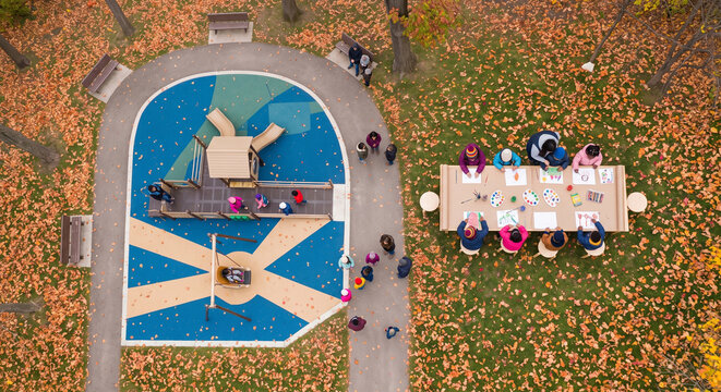 Aerial view of children activities in a bright blue playground and drawing together at a long outdoor table surrounded by fallen orange leaves