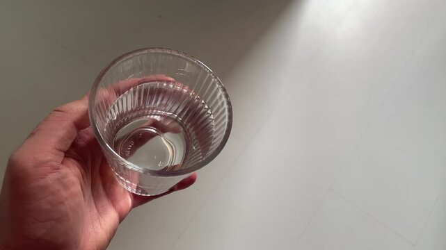 Man Hand Holding Glass of Fresh Pure Water against Light Background