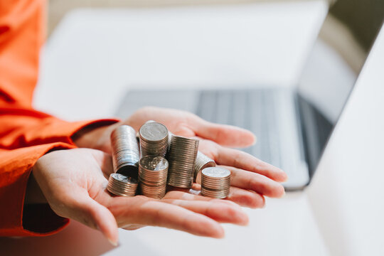 Hands holding stack coin with laptop in background, savings concept and finance growth