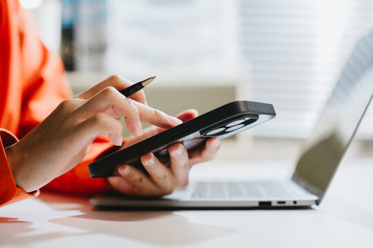 Person using tablet near laptop in bright office workspace, close up hand holding tablet and pen