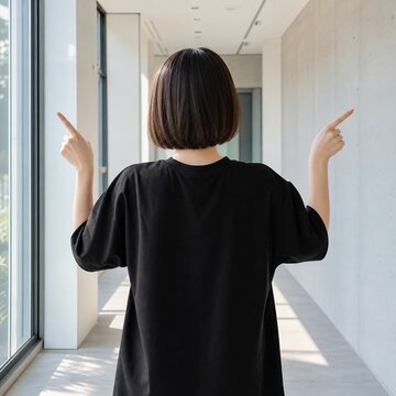 Woman wearing a plain black t-shirt stands in a modern hallway while pointing her fingers toward empty walls on both sides.