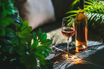 Obraz premium Pink rose wine glass on table surrounded by tropical plants. Green oasis restaurant lounge zone and luxury summer vacation relaxation concept.