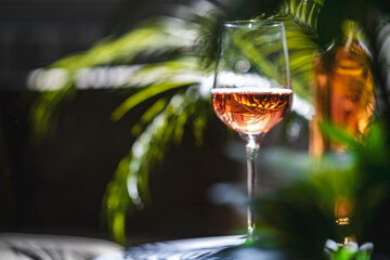 Obraz premium Pink rose wine glass in front of blurry bottle. Tropical lounge bar atmosphere and organic winemaking brand advertisement concept.