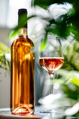 Obraz premium Premium rose wine bottle and glass in tropical greenery. Luxury eco resort restaurant card and organic summer winemaking concept.