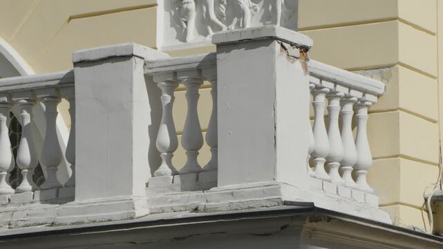 A classic white balustrade with ornate balusters sits on the balcony of a historical yellow building during a bright sunny day.