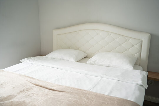 Minimalist bedroom with white upholstered headboard and simple bedding. Home decor interior design and real estate staging