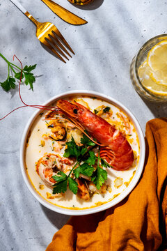 Seafood chowder soup with langoustine, mussels in bowl with cutlery, napkin on background. Vertical top view gourmet menu background, Mediterranean seafood restaurant concept.