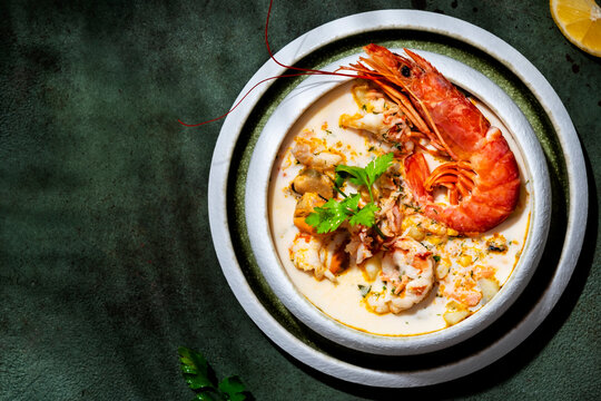 Creamy seafood chowder soup with big prawn, and mussels captured in hard light. Luxury restaurant delicacy, set on dark green background for menu design.