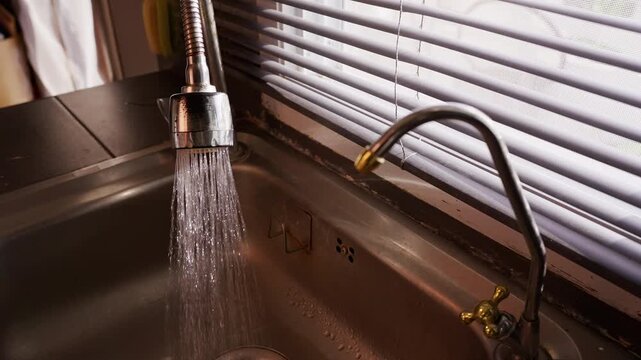 Person Turns On Kitchen Faucet and Water Begins Flowing into Metal Sink in Slow Motion, Household Routine and Water Consumption