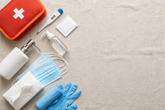 A first aid kit sits next to various medical items such as gloves, masks, and a thermometer. The supplies are organized on a plain surface. This setup indicates readiness for health emergencies