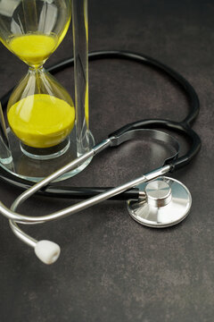 Stethoscope beside an hourglass on a dark surface. Concept of healthcare, medical care, time management, emergency response, patient care and health monitoring.