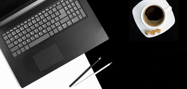 Office desk with laptop and and coffee cup on a black background. Top view. Copy space.