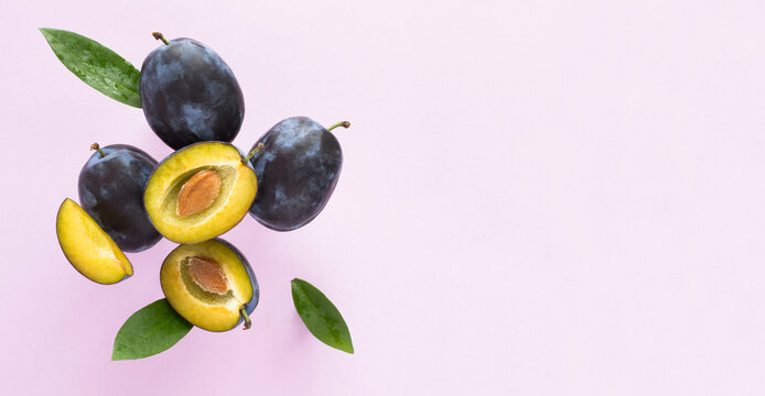 Flying in air fresh ripe whole and cut blue plums with leavs on a pink background. Top view. Copy space.