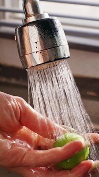 Vertical video. Close View of Female Hand Washing Green Lime beneath Faucet Spray in Slow Motion, Food Hygiene and Fresh Produce Preparation