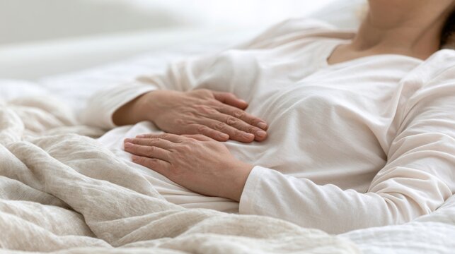 Woman practicing diaphragmatic breathing while resting in bed with hands on chest and abdomen. Relaxation technique for stress relief and better sleep
