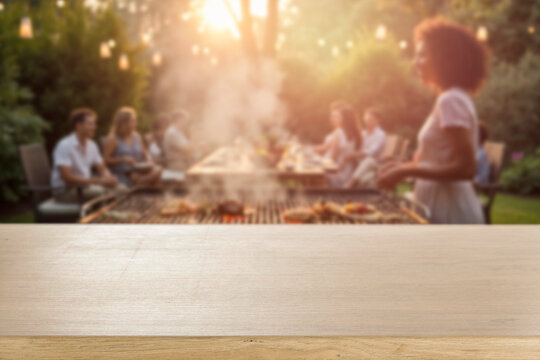 Empty wooden table for product placement. Blurred background with friends and family gathered in garden enjoying summer barbecue on sunny day. 