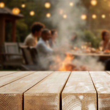 Empty wooden table for product placement. Blurred background with friends and family gathered in garden enjoying summer barbecue on sunny day. 
