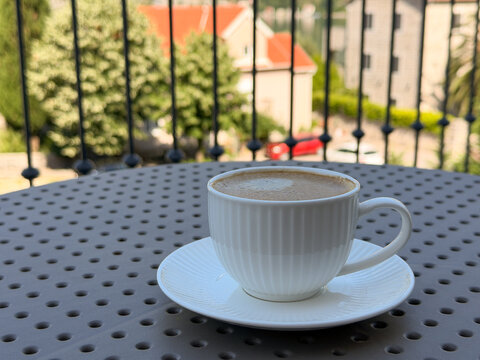 Cup of cappuccino on a small balcony table overlooking a historic narrow street, European travel and relaxed lifestyle concept
