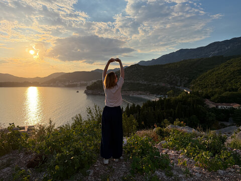 Woman standing on high rocky Adriatic Sea coast illuminated by golden sunset light, dramatic Mediterranean landscape and travel freedom conceptconcept