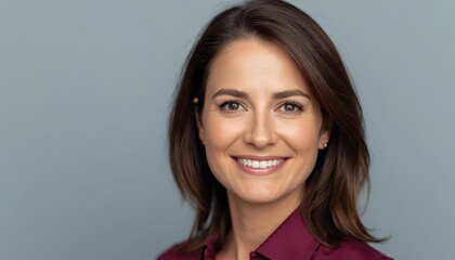 Fototapeta premium Isolated portrait of smiling middle-aged woman on grey background, wearing maroon shirt and looking at the camera. Attractive mature latin businesswoman, professional business executive entrepreneur