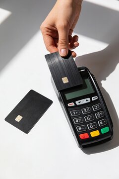 Person using contactless card payment terminal with modern credit card on white surface