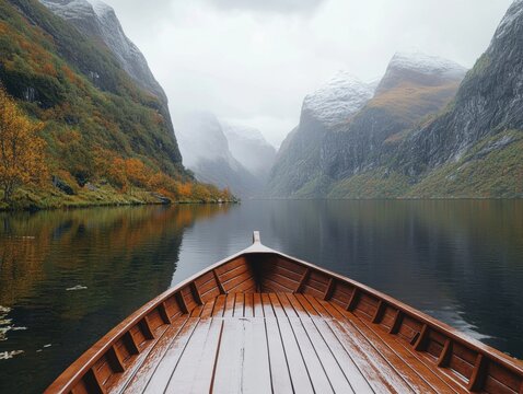 A point-of-view shot from the bow of a wooden boat looking forward onto a calm, glassy lake toward distant misty mountain valleys.