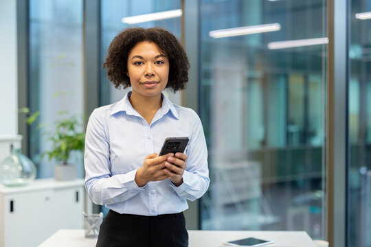 Portrait of an African American businesswoman standing in the office, holding a phone and looking at the camera